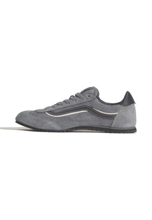 Grijze suède vetersneaker met zwarte en witte zijstreep en zwarte rubberen zool, zijaanzicht op witte achtergrond.
