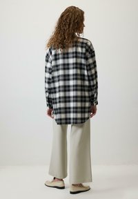 Crna i bijela karirana flanel košulja s dugim rukavima, uparena s laganim bež hlačama širokih nogavica i bež mokasinkama.