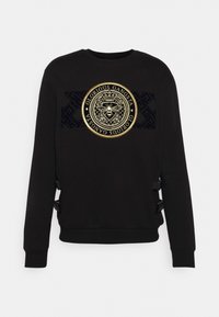 Felpa nera con un logo circolare in oro embossato, caratterizzato da un design di ape e dettagli in tessuto testurizzato sulla parte anteriore e sui cinturini laterali.