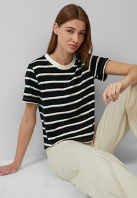 T-shirt à manches courtes noir et blanc à rayures, avec un col rond, fabriqué en coton doux ; présenté avec un pantalon clair.