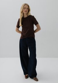 Ciemnobrązowa koszulka z krótkim rękawem zestawiona z luźnymi, ciemnoniebieskimi spodniami o szerokich nogawkach oraz brązowymi butami na szpilce. Minimalistyczny design, gładki materiał i luźny krój.