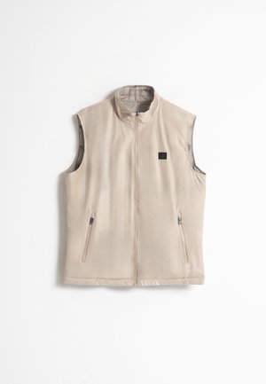 Chaleco sin mangas color beige, hecho de tejido suave, con cuello alto, cierre frontal y dos bolsillos laterales. Logo sutil en la zona del pecho.