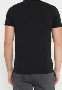 Camiseta de algodón negra, de mangas cortas, con cuello redondeado, forma ajustada, textura suave, diseño liso. Costura visible en el cuello y el dobladillo.