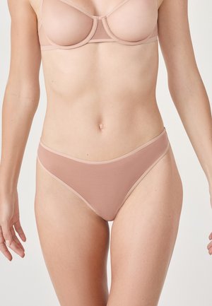 Tanga de color nude, hecha de tejido suave, con una textura lisa y un sutil ribete de contraste a lo largo de la cinturilla y las aberturas de las piernas.