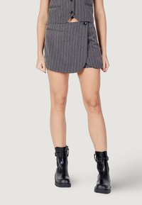 Gonna grigia a righe sottili con pannelli sovrapposti sul davanti, abbinata a un gilet coordinato. La modella indossa stivaletti neri con fibbie decorative.