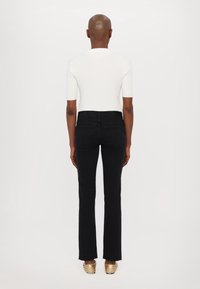 Svarta denimflare jeans med rå nederkant, tillsammans med en åtsittande vit ribbad t-shirt med korta ärmar och gyllene glidskor. Slät textur.