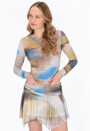 Tânără cu păr lung ondulat, purtând un top cu mâneci lungi, colorat, cu model abstract, și o fustă asimetrică asortată.