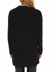 Svart ribbad stickad tröja med rund hals och långa ärmar, med en hög-låg nederkant och subtil textur. Avslappnad och ledig passform.