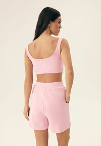 Różowy zestaw sportowy składający się z topu na ramiączkach z okrągłym dekoltem i dopasowanych szortów z elastycznym pasem oraz bocznymi kieszeniami. Miękka, elastyczna tkanina.