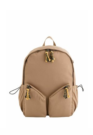 Beiger Rucksack mit zwei Frontreißverschlusstaschen und schwarz-gelben Kordel-Zipperanhängern, plus Seitentaschen und einer oberen Griffschlaufe.
