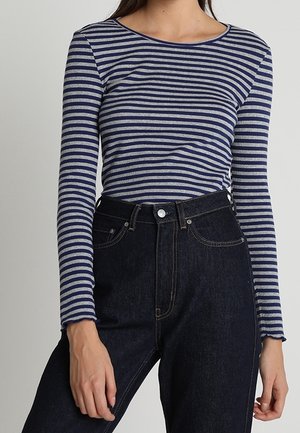 Top met lange mouwen met horizontale marineblauwe en grijze strepen, gemaakt van zachte stof, met een ronde hals en een getailleerd silhouet, gedragen met donkere jeans.