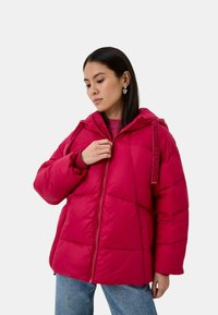 Giacca puffer fucsia con cappuccio, caratterizzata da un design trapuntato e polsini elastici. Chiusura con zip e dettaglio con tracolla brandizzata.
