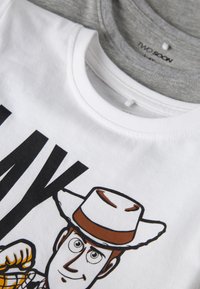 Gros plan sur des t-shirts à col rond empilés, blancs et gris, le t-shirt blanc étant imprimé d'un personnage de cowboy de dessin animé portant un chapeau marron et blanc.