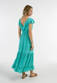Rochie maxi teal cu spate în V, mâneci volan și talie strânsă. Design cu straturi și fustă fluidă. Purtați cu sandale plate.