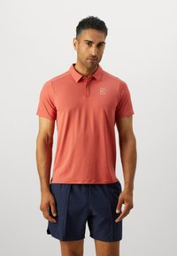 Korteermet polo skjorte i korall, lavet af åndbart materiale, med knaplukning og logo på brystet, parret med marineblå shorts.