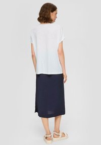 Hellgraues T-Shirt mit kurzen Ärmeln in lockerem Schnitt, kombiniert mit einem dunkelblauen, knöchellangen Rock mit einem seitlichen Schlitz. Dazu werden beigen Sandalen getragen.