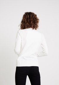 Biały, długi sweter dzianinowy z dopasowanym krojem i prążkowanym wykończeniem. Tył ma gładką fakturę i klasyczny okrągły dekolt.