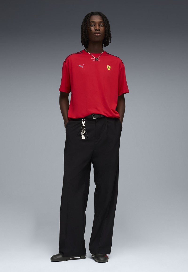 Punane lühikeste varrukatega särk Puma ja Ferrari logodega, mustade laia lahaga pükste ja mustade kingadega. Riietust kaunistavad hõbedased kettdetailid.