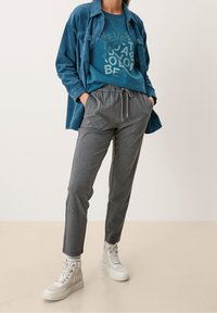 Felpa teal con testo grafico, indossata sotto una camicia in velluto a coste blu a righe. Pantaloni jogger grigi e sneakers alte color crema.