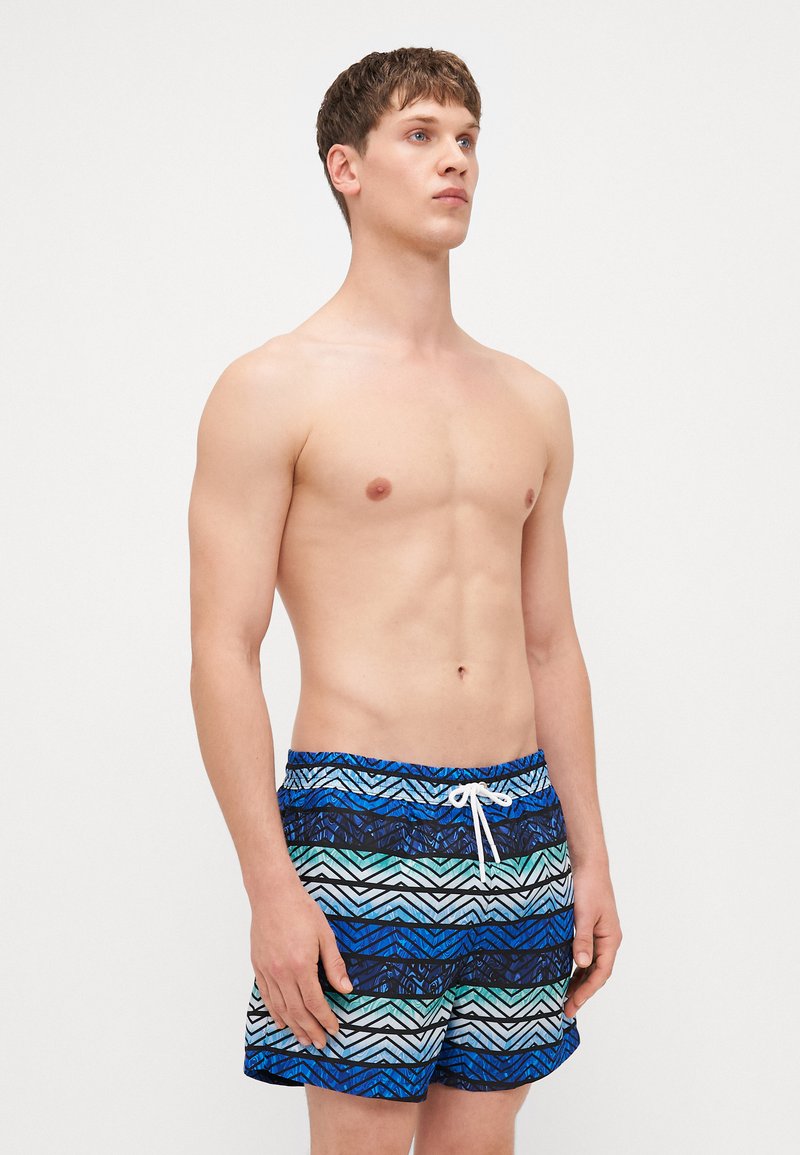 Badeshorts in Blau mit Zickzackmuster, ausgestattet mit einem Kordelzugbund und kontrastierenden weißen Besätzen. Hergestellt aus leichtem, atmungsaktivem Material.