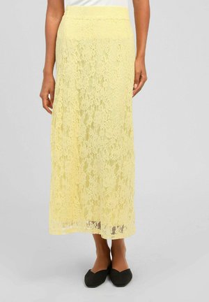 Jupe midi en dentelle florale jaune portée avec des ballerines noires, montrée de la taille aux pieds sur fond neutre.