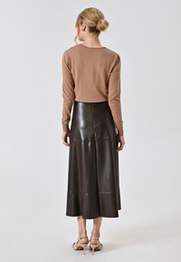 Braunes Langarmoberteil kombiniert mit einem langen, dunkelbraunen Lederrock. Der Rock hat einen ausgestellten Saum und eine glatte Textur. Elegante Sandalen sind sichtbar.