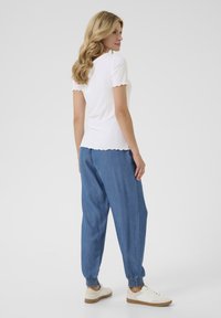 Un top alb cu dungi, cu mânecă scurtă și margini ondulate, asortat cu pantaloni joggeri lejeri din denim albastru și adidași albi. Un outfit casual.
