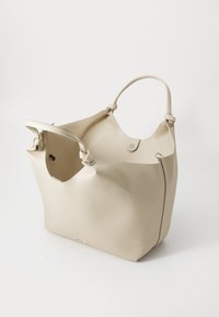 Beige skinnveske med en strukturert design, åpen topp, to håndtak og en subtil logo nederst. Glatt tekstur og minimalistiske detaljer.