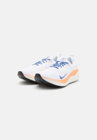Scarpe sportive bianche con tomaia testurizzata, lacci blu e dettagli arancioni sulla parte intermedia. Suola in gomma nera per la trazione.