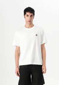 Balta medvilnė t-shirt su apvalia iškirpte, trumpomis rankovėmis ir mažai išsiuvinėta dviračio su banglente dizainu ant krūtinės.