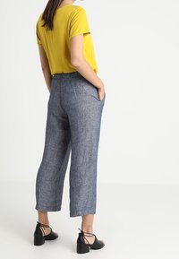 Top giallo a maniche corte abbinato a pantaloni in lino blu a gamba larga e lunghezza caviglia. Sandali neri con cinturini completano l'outfit.