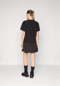 T-shirt de algodão preto com mangas curtas, combinado com uma saia escura. Modelo usa ténis pretos e meias. Fundo neutro.