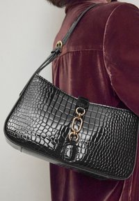 Sac à main en similicuir noir avec une texture crocodile, un accent en chaîne dorée et une bandoulière réglable. Forme structurée avec une finition brillante.