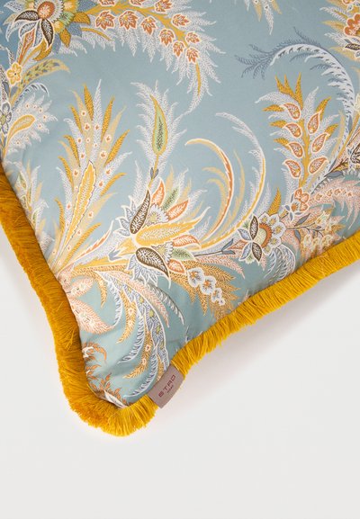 Coussin décoratif avec franges jaune moutarde et tissu bleu pâle présentant des motifs botaniques complexes en nuances d'orange, blanc et vert.