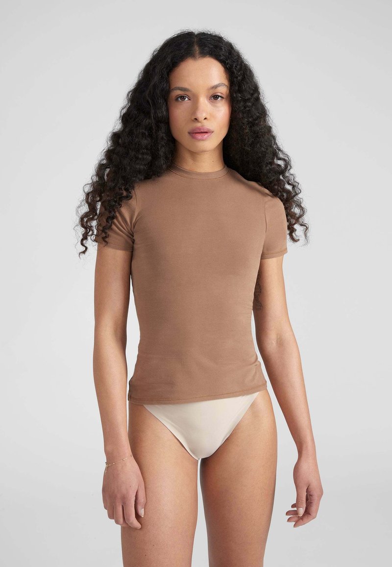 Braun passendes Kurzarmoberteil aus weichem Material mit Rundhalsausschnitt, kombiniert mit beigen hochgeschnittenen Hosen. Glatte Textur und minimales Design.