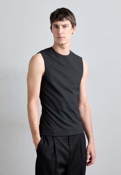 Camiseta sin mangas negra con un escote redondo, hecha de una tela suave. Diseñada con una silueta ajustada y costuras mínimas. Llevada con pantalones negros.