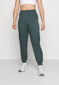 Donkergroene joggers met een elastische tailleband, manchetvoeten en zijzakken. Gecombineerd met witte sportschoenen, wat een casual uitstraling geeft.