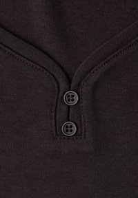 Mørkebrunt bomuldsstof med V-hals-design og to sorte knapper nær halsudskæringen. Glat tekstur med subtile syninger.