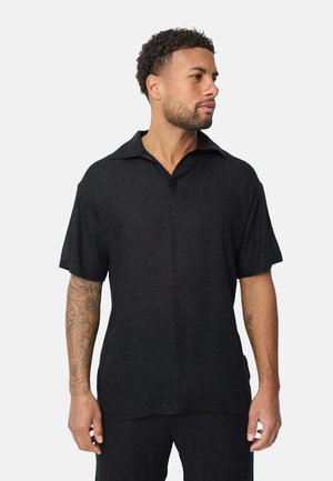 Chemise noire à manches courtes avec un col, en tissu léger, à coupe décontractée, et un bouton unique au niveau de la poitrine.