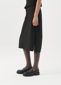 Μαύρη φούστα έως το γόνατο με πλάγιο σκίσιμο, σε συνδυασμό με μαύρους loafers και διάφανες καφέ καλσόν, με απαλό ύφασμα και απλό σχέδιο.