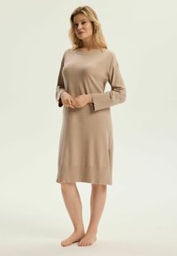 Beżowa dzianinowa sukienka z długimi rękawami, okrągłym dekoltem, rozcięciami po bokach oraz prążkowanym wykończeniem u dołu i na mankietach. Model maxi.