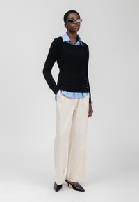 Zwarte aansluitende trui, lichtblauw gestreept overhemd met kraag, crème wijde broek en zwarte gestroomde muiltjes. Eenvoudig ontwerp, gladde textuur.