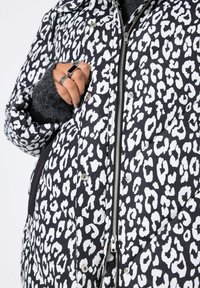 Chaqueta acolchada con estampado de leopardo en blanco y negro, que presenta un cierre de cremallera y botones a presión, con tejido texturizado y puños en contraste.