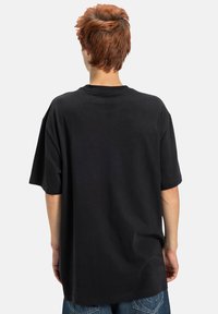 Čierne oversized tričko z bavlny, s krátkymi rukávmi, okrúhlym výstrihom a voľným strihom. Hladká textúra bez viditeľných vzorov alebo akcentov.