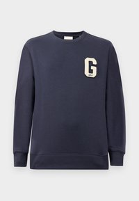 Mørkeblå hettegenser laget av bomullsblanding, med ribbestrikket hals og mansjetter, og et kremfarget "G"-merke på brystet.