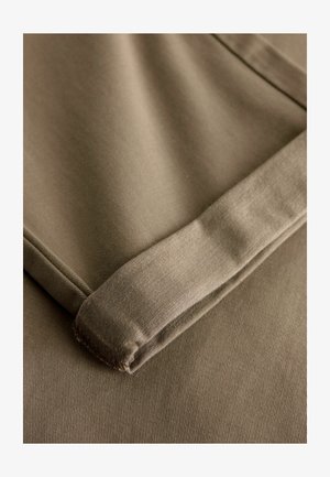 Tela de algodón beige doblada con una textura suave, que presenta un borde nítido y un patrón sutil de canalé; aspecto suave y flexible.