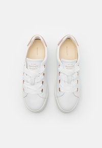 White sneakers made of smooth leather with a minimalist design. Features flat white laces, rose gold eyelets, and a beige insole.