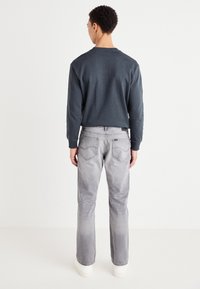 Camisa gris de manga larga con cuello redondo, combinada con jeans gris claros. Los jeans cuentan con bolsillos traseros y un corte holgado, usados con zapatillas blancas.