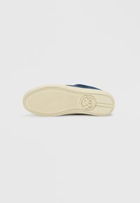 Σόλα αθλητικού παπουτσιού με ελαφρύ κρεμ χρώμα από καουτσούκ στο κάτω μέρος με υφή για καλύτερη πρόσφυση, στρογγυλό διακοσμητικό λογότυπο και μπλε σκούρο επάνω μέρος ορατό στη φτέρνα.