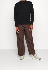 Pull noir en maille, pantalon cargo marron et baskets beiges. Le pull a un col côtelé, tandis que le pantalon présente une coupe ample et des poches.
